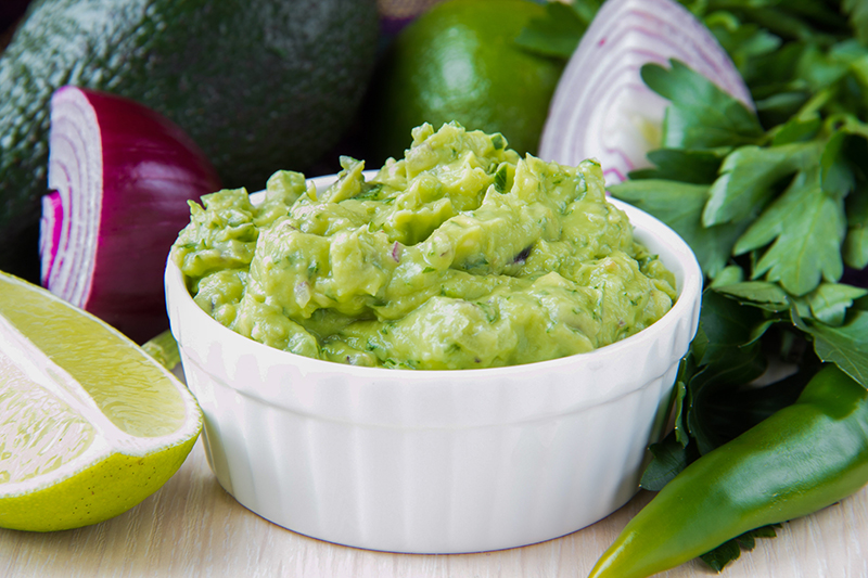 Green Mexican guacamole dip with avocado, lime, parsley and red